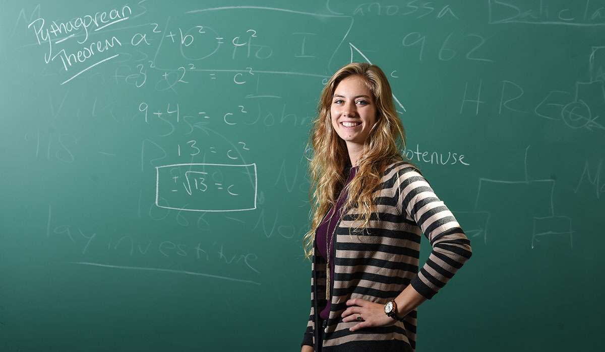 Student standing in front of board with math equation